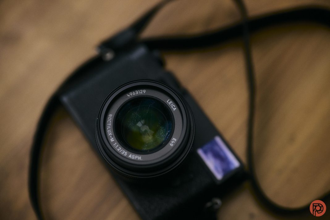 A black Leica camera with a lens and strap rests on a wooden surface.