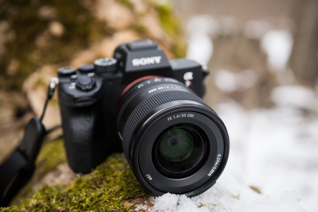 The Best Prime Lenses to Pick Today for Your Sony A Sony camera with a large lens rests on mossy ground with some snow in the background.
