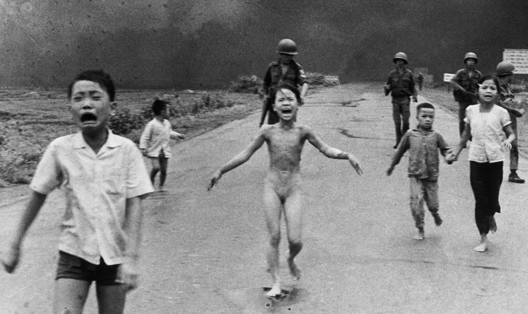 The 'Terror of War' Authorship Conversation Should Go Far Beyond A group of children, some crying and barefoot, run down a road toward the camera with smoke and armed soldiers in the background. The central child appears distressed and unclothed.
