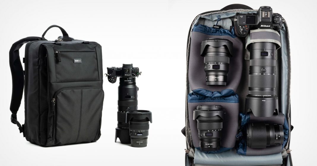 A black camera backpack is shown next to a camera and three lenses. The bag is open, revealing organized compartments with a camera body attached to a lens, plus three additional lenses.