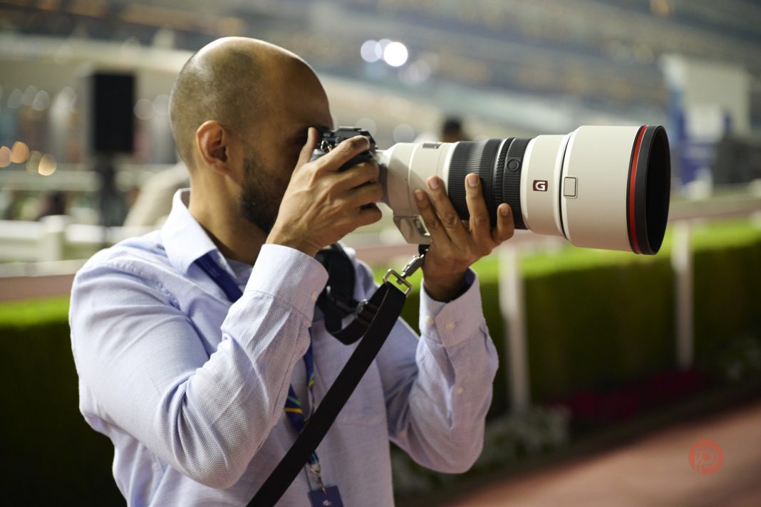 This Arabic Concept Reveals What’s Missing in Photography Today Person in a blue shirt using a large camera with a telephoto lens in an outdoor setting.