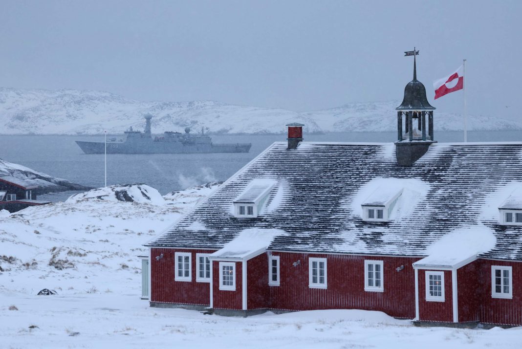 Touching down in Nuuk, ground zero for the world’s most NUUK, GREENLAND - JANUARY 18: The Greenlandic flag flies over a building as the HDMS Vaedderen frigate of the Danish Navy patrols behind on January 18, 2026 in Nuuk, Greenland. Greenlandic, Danish and other European leaders are hoping they can still avert an intervention by the United States to forcefully acquire the island as U.S. President Donald Trump continues to insist the U.S. must have Greenland, suggesting even by military means if necessary. (Photo by Sean Gallup/Getty Images)