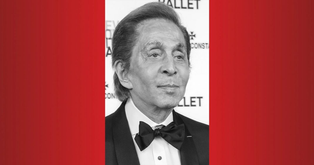 A man with neatly styled hair wearing a black tuxedo and bow tie poses in front of a backdrop at an event; the photo is in black and white with red borders on each side.