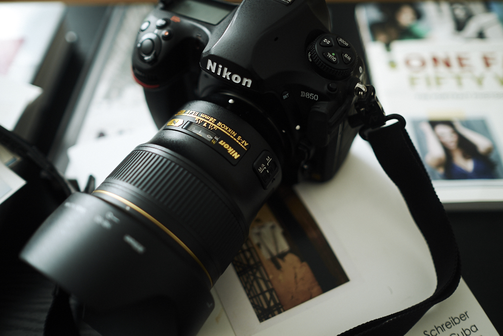 Get this Nikon DSLR before it Becomes More Expensive Close-up of a Nikon DSLR camera on a table with scattered papers and books in the background.