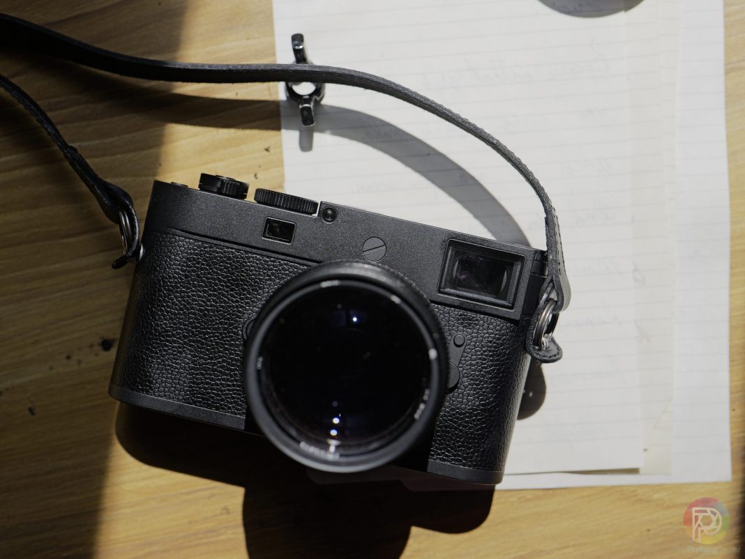 The Best Leica Cameras With Jaw-Dropping Dynamic Range A black camera with a strap rests on handwritten papers on a wooden surface in sunlight.