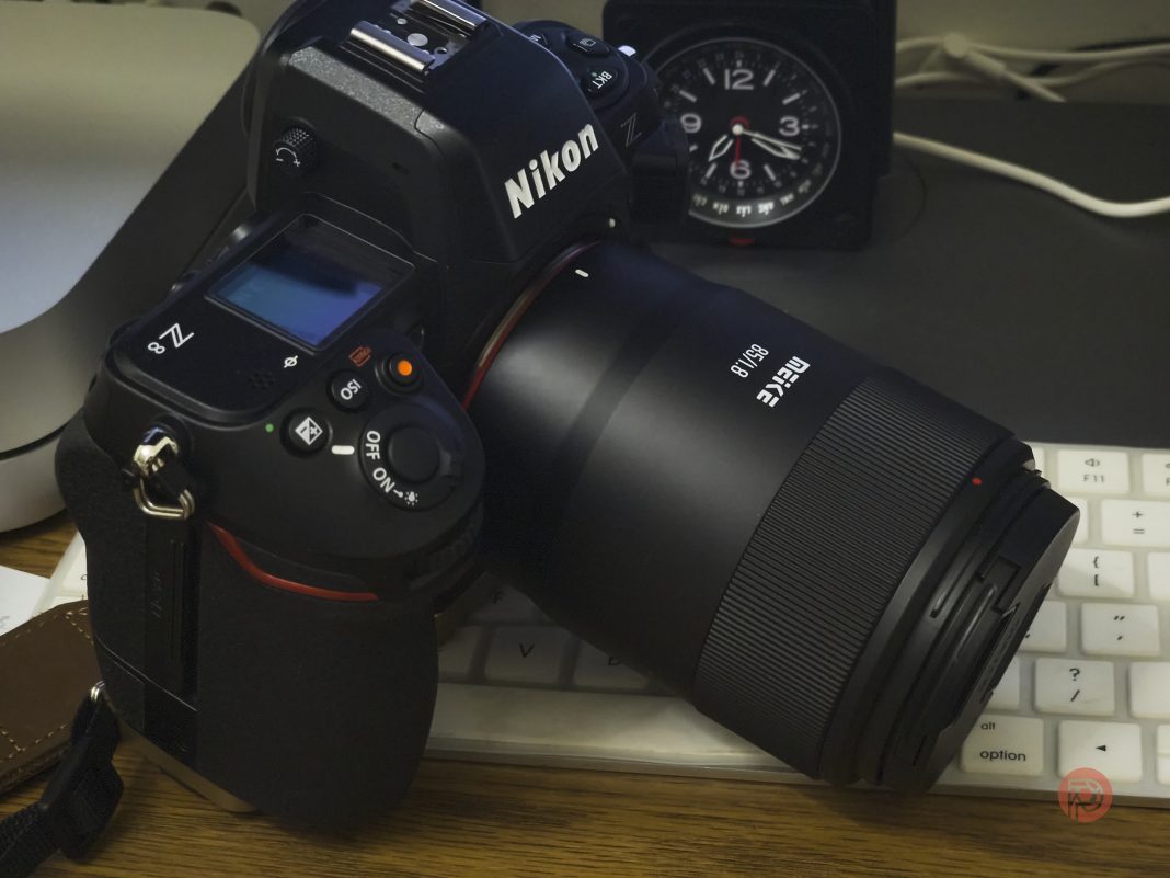 The Meike 85mm f1.8 Mark II is Great for Two A Nikon Z camera with a large lens rests on a white keyboard near a computer and a clock.
