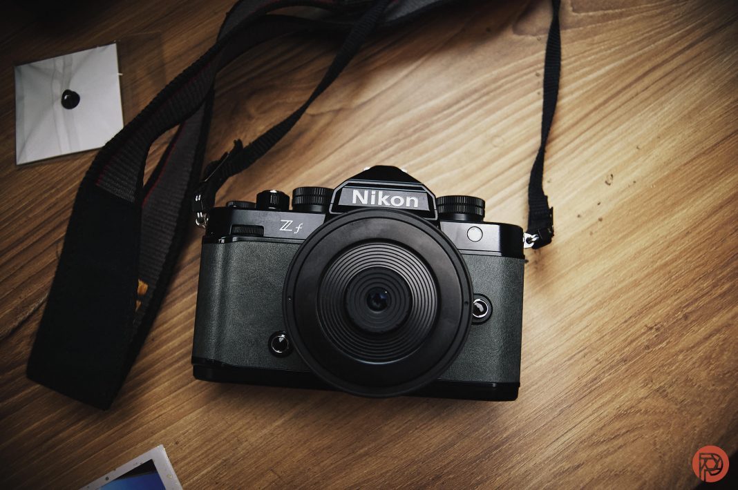 The Squint and Shoot Experience A Nikon Z fc camera with a wide lens sits on a wooden surface, strap and photo prints nearby.