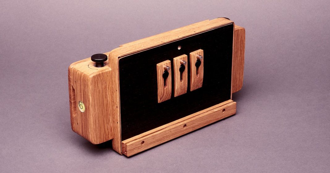 The World's First Modular Pinhole Camera System Is Now Available A handcrafted wooden camera with black panels and three toggle switches on the front, placed on a plain background. The design combines natural wood with functional hardware elements.
