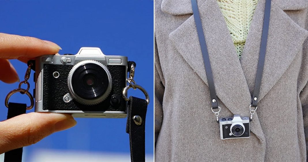 This Teeny-Tiny Retro-Inspired Camera Is So Darn Cute A miniature camera is shown in two scenes: held between fingers against a blue sky, and worn as a necklace over a brown coat.