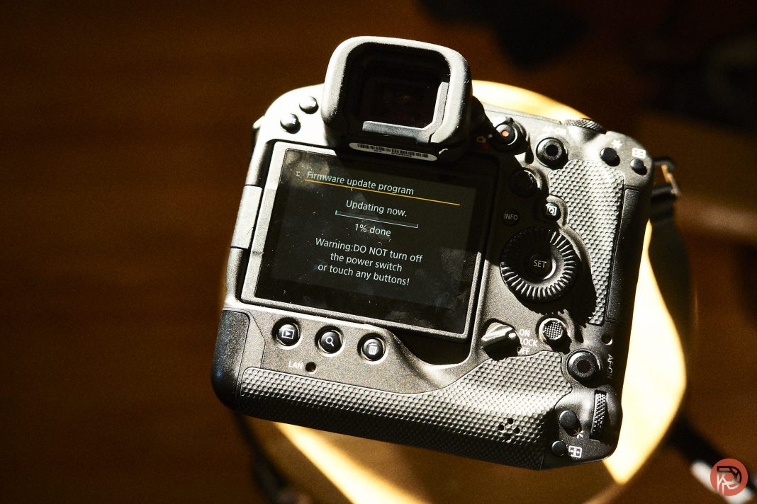 A digital camera displays a firmware update screen, warning not to turn off the power switch.
