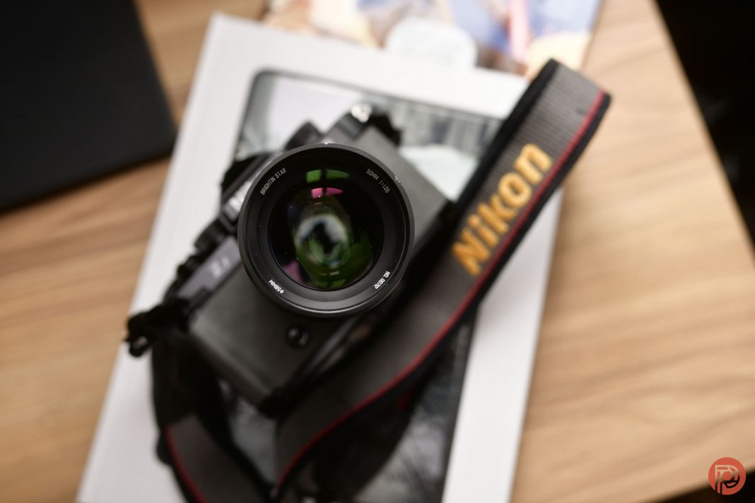 The 1 Reason it Beats the Noct A Nikon camera with a lens and strap rests on a book on a wooden surface.