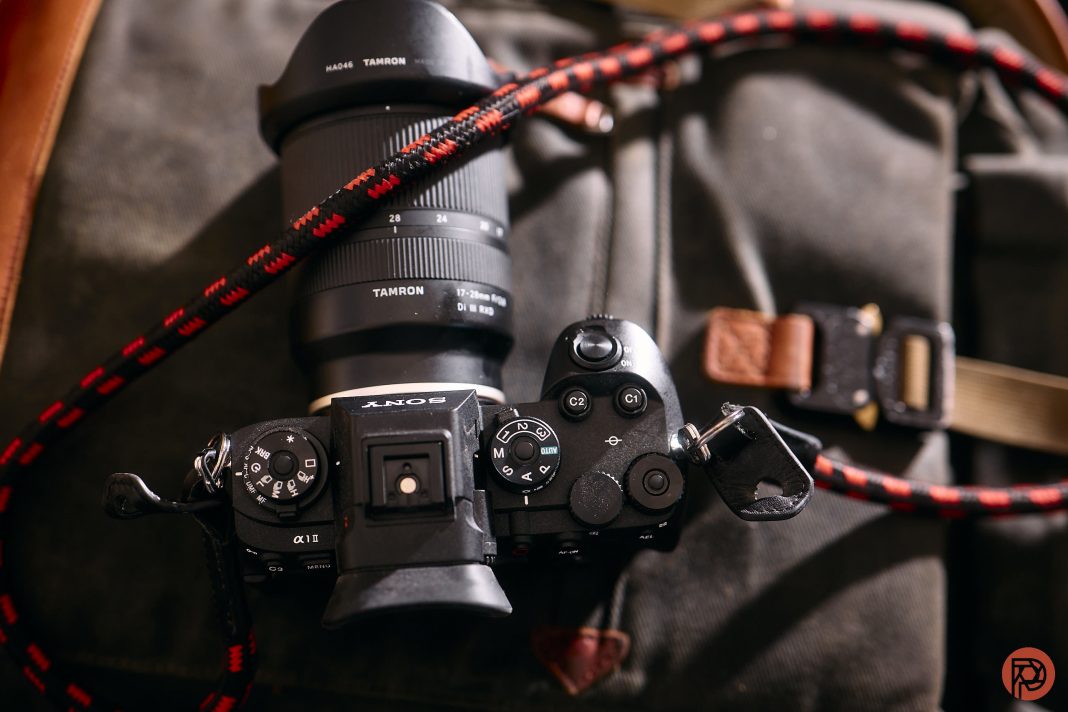 Sony camera with Tamron lens and red-black strap resting on a dark fabric bag.